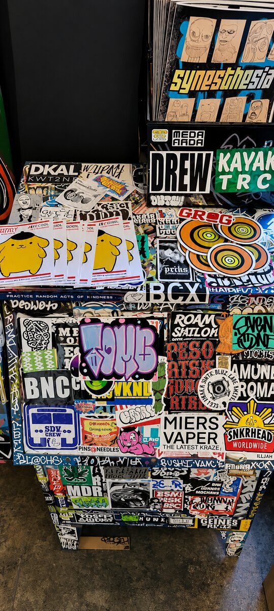 A sticker-covered display and zine rack at VISUAL